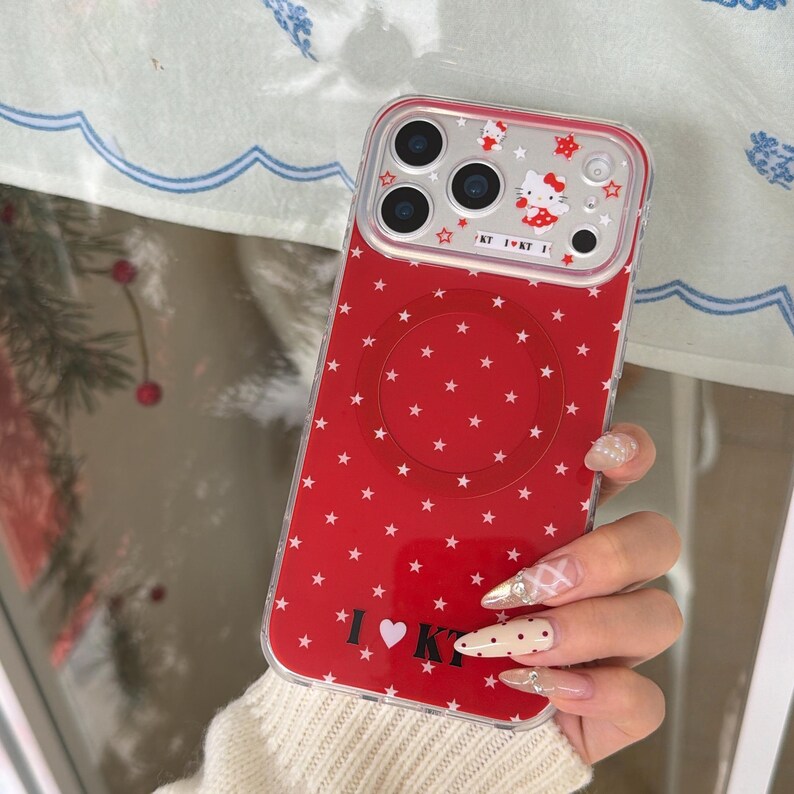 May include: Red phone case with a white star pattern and a clear top section. The top section features a cartoon character and the text "KT I KT I". The case has a circular design on the back and the text "I &hearts; KT".