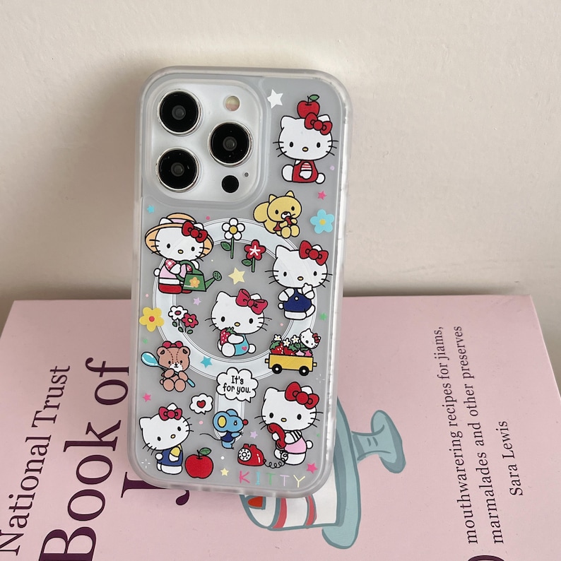 May include: Clear phone case featuring a colorful Hello Kitty design. The case has multiple illustrations of Hello Kitty in various poses, along with flowers, stars, and other cute elements. The word "KITTY" is printed at the bottom.