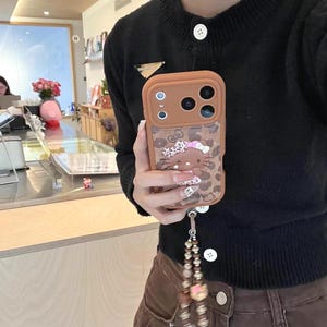 Läderfodral i rosa brunt leopardmönster med Hello Kitty-motiv och snodd för iPhone 17 Pro, 16 Pro Max och 15-serien. bild 1