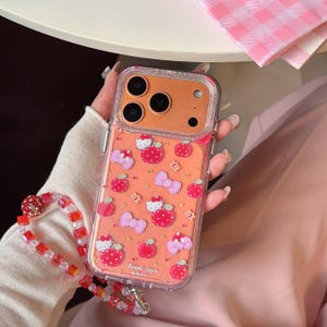 May include: Clear phone case with an orange background featuring red apples, pink bows, and the text "Simple Apple". The case has a decorative red and clear beaded wrist strap.