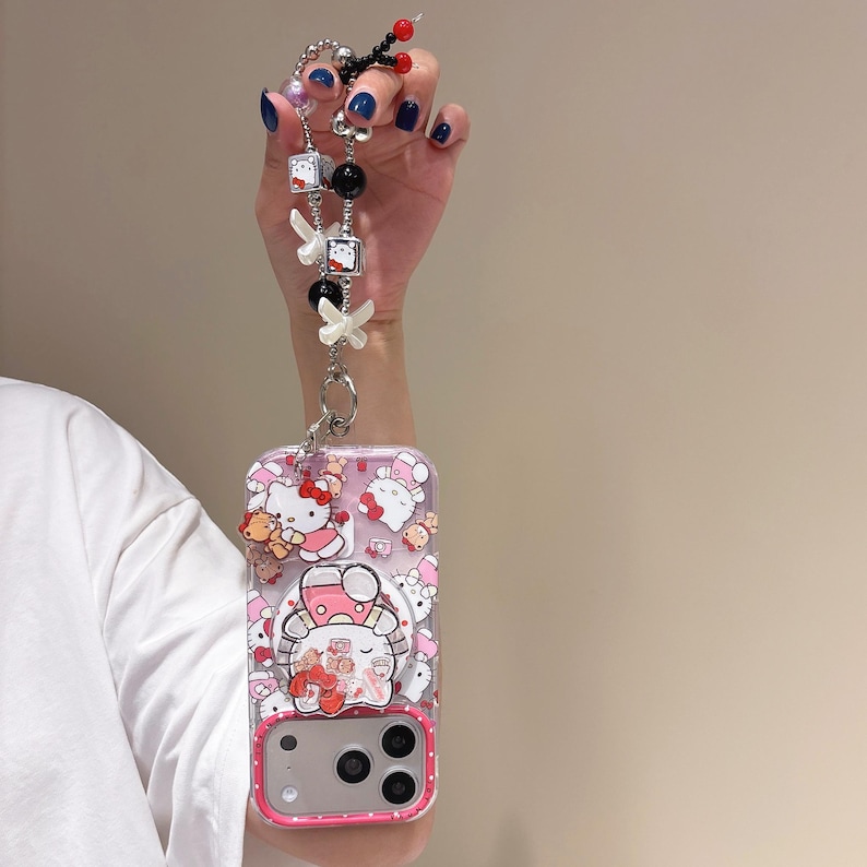 May include: Clear phone case with a pink border featuring Hello Kitty characters. The case is attached to a beaded lanyard with white bows, black and silver beads, and Hello Kitty charms.