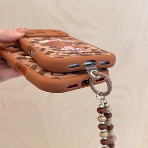 Läderfodral i rosa brunt leopardmönster med Hello Kitty-motiv och snodd för iPhone 17 Pro, 16 Pro Max och 15-serien. bild 4