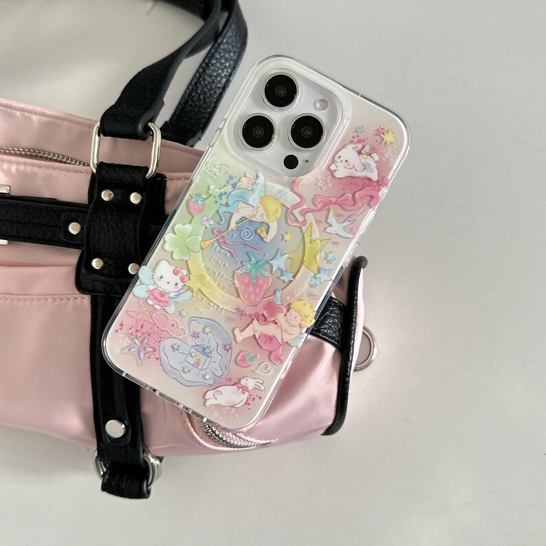 May include: Clear phone case with a colorful, whimsical design featuring cherubs, stars, a crescent moon, and strawberries. The case is resting on a pink handbag with black straps.