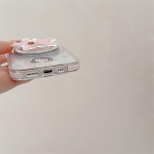 K&ouml;nnte beinhalten: Transparente Handyh&uuml;lle mit einem rosa schleifenf&ouml;rmigen Handyhalter. Die H&uuml;lle hat einen rosa Rand und ein Cartoon-Charakter-Design. Die H&uuml;lle ist f&uuml;r ein Smartphone konzipiert.