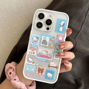 Puede incluir: Funda transparente para tel&eacute;fono con borde blanco, decorada con pegatinas coloridas con personajes de dibujos animados. Las pegatinas incluyen im&aacute;genes de Hello Kitty, conejos y osos. El texto "Lovely Kitty" y "Hello" es visible en la funda.