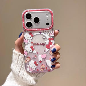 May include: Clear phone case with a pink border and a Hello Kitty design. The case features multiple Hello Kitty illustrations, hearts, and other cute graphics. The text "Hello Kitty" is also visible on the case.