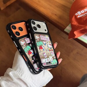 May include: Two black phone cases with a clear back featuring a colorful Hello Kitty design. The cases have a black border and a clear back with various Hello Kitty illustrations. One case has an orange camera area, the other has a white camera area.