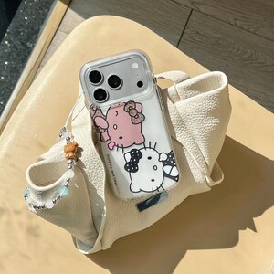 May include: A clear phone case featuring a pink and white cartoon character design. The case is on a white leather bag with a beaded wrist strap. The phone case has the text "Enjoy the good times."