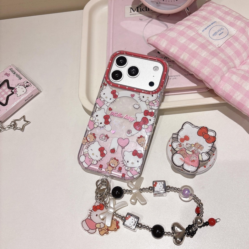 May include: A selection of Hello Kitty themed items, including a phone case, pop socket, bracelet, and small box. The phone case has a red border and is decorated with Hello Kitty motifs. The bracelet features black beads and silver charms.
