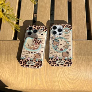 May include: Two clear phone cases with a leopard print design and illustrations of a cartoon cat and teddy bears. One case has a heart-shaped element with floating glitter. The cases have text that reads "KITTY."