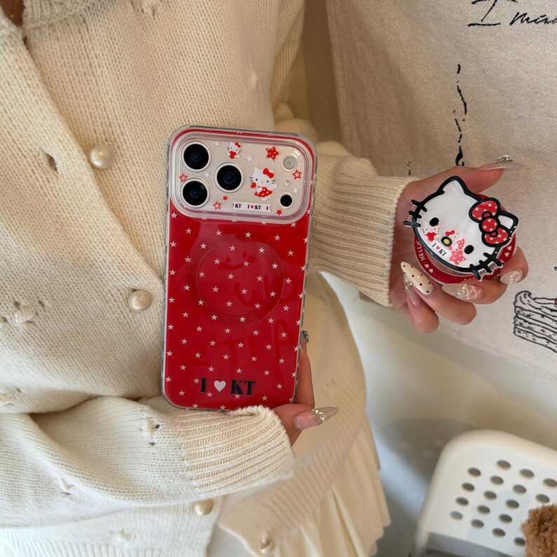May include: Red phone case with white star pattern and a clear pop-up grip. The case features a Hello Kitty design and the text "I ❤️ KT". A matching pop-up grip with a Hello Kitty design is also visible.