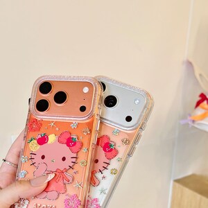 May include: Two clear phone cases with a Hello Kitty design. The cases have a pink and orange color scheme with a glittery border. The Hello Kitty design includes a pink bow, strawberries, and the word "Aloha".