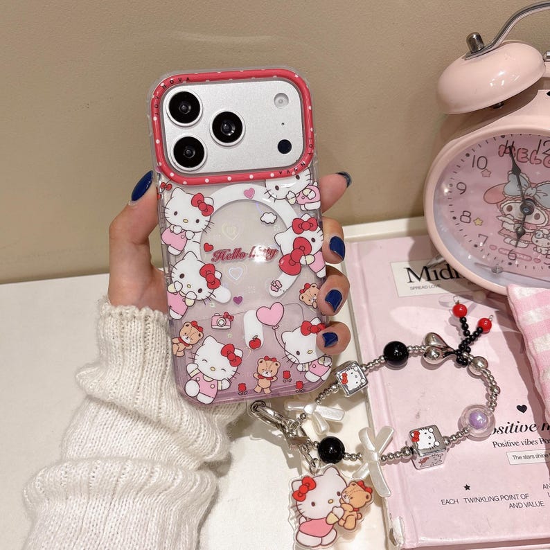 May include: A clear phone case with a pink trim, decorated with Hello Kitty characters and a matching charm bracelet. The case features a repeating pattern of the character with bows and teddy bears. The charm bracelet has black beads and Hello Kitty charms.