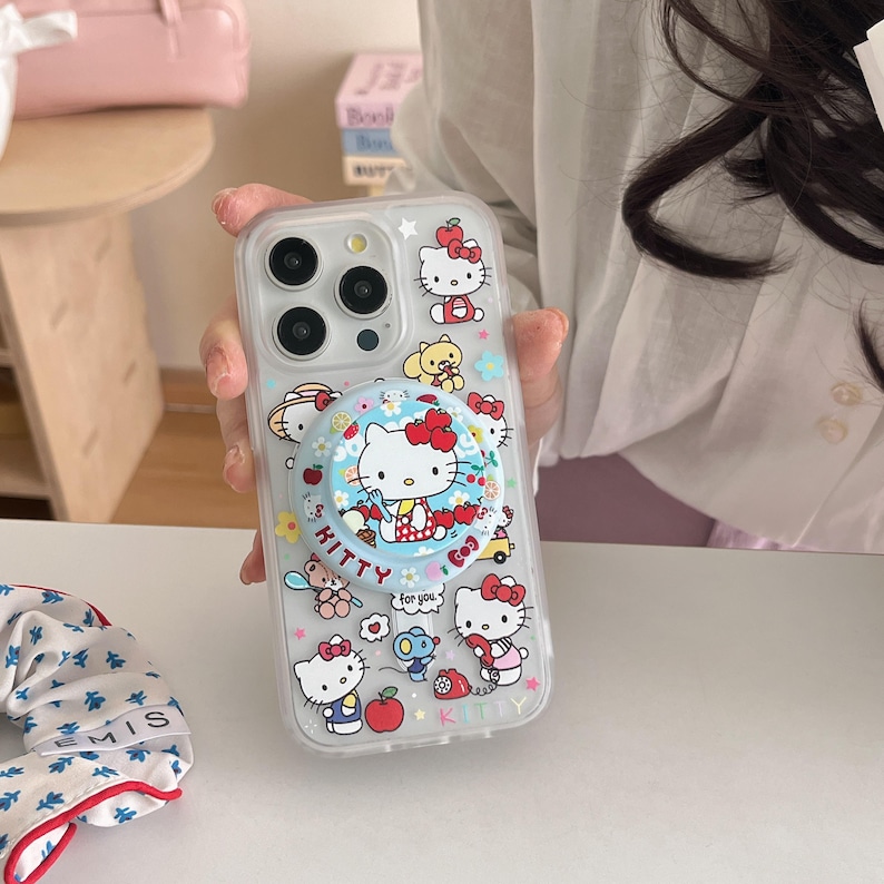 May include: Clear phone case with a pop-up grip featuring Hello Kitty characters. The case has a variety of Hello Kitty illustrations, including the character with a red bow. The pop-up grip has the text "Kitty" and "for you".