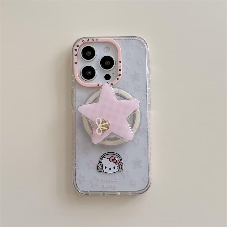 K&ouml;nnte beinhalten: Transparente Handyh&uuml;lle mit einem rosa sternf&ouml;rmigen Handyhalter und einem Hello Kitty-Motiv. Die H&uuml;lle hat einen rosa Kamerarand und einen wei&szlig;en Ringhalter. Der Hintergrund hat ein Muster aus kleinen Sternen.