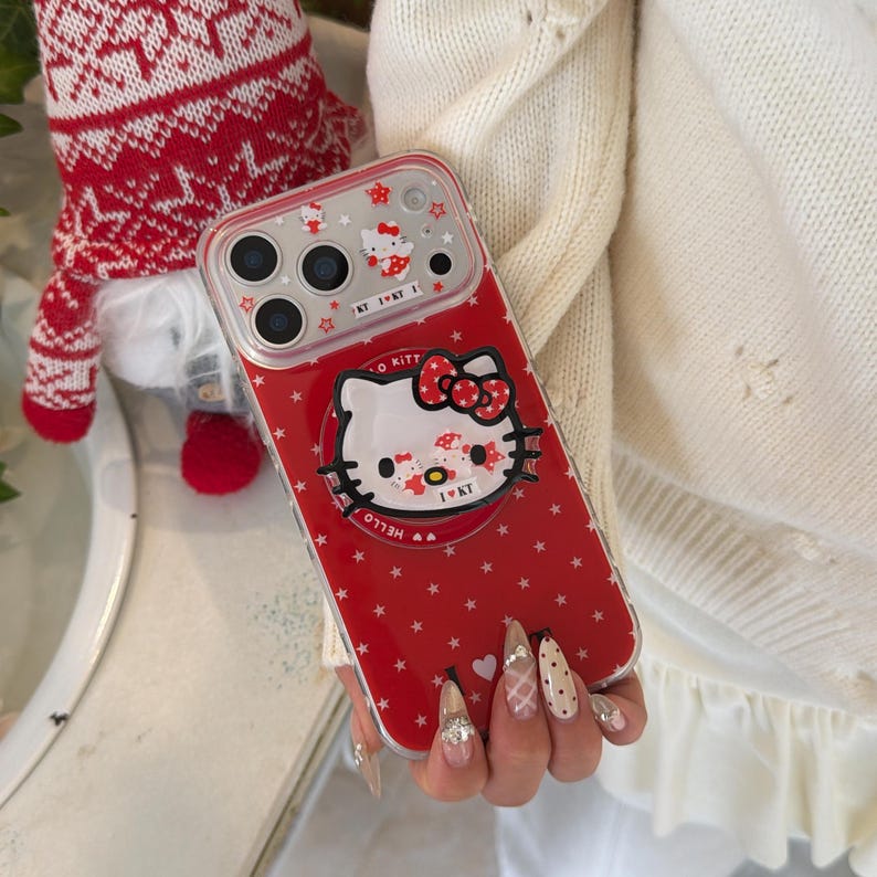 May include: Red phone case featuring a Hello Kitty design with a red bow and star pattern. The case has a clear border and includes the text "Hello Kitty" and "I ♡ KT".