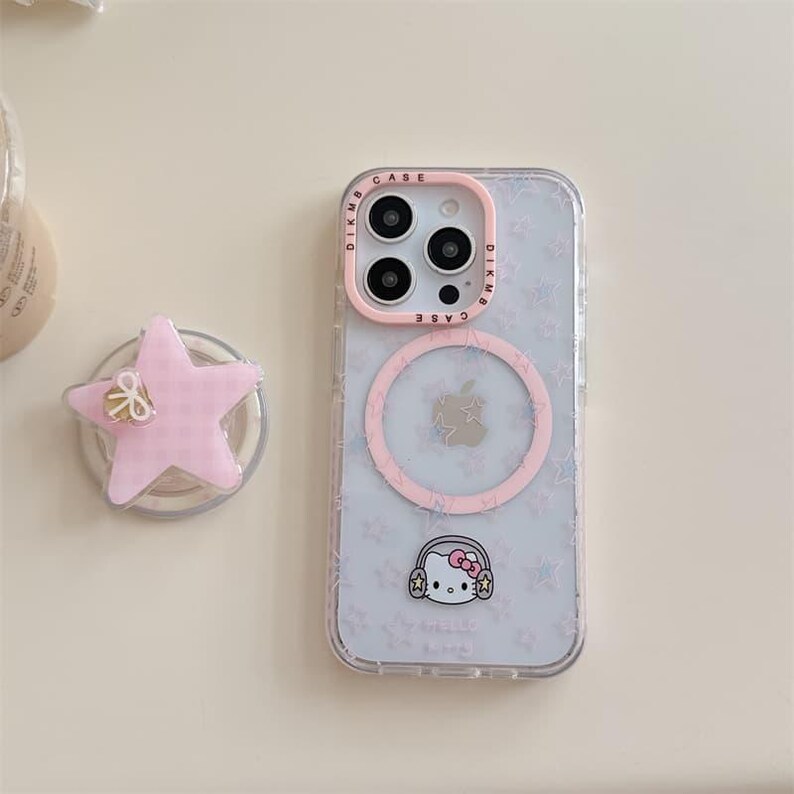 K&ouml;nnte beinhalten: Eine transparente Handyh&uuml;lle mit rosa Rand und Hello Kitty-Design. Die H&uuml;lle hat einen rosa Kreis und ein Sternmuster. Ein rosa sternf&ouml;rmiger Handyhalter befindet sich neben dem Telefon.