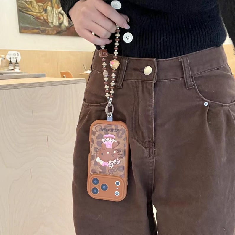Läderfodral i rosa brunt leopardmönster med Hello Kitty-motiv och snodd för iPhone 17 Pro, 16 Pro Max och 15-serien. bild 3