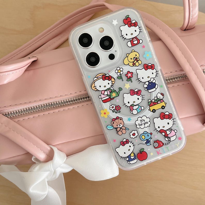 May include: Clear phone case featuring a colorful Hello Kitty design with various poses and accessories. The case is decorated with flowers, stars, and the phrase "It's for you." The case is shown next to a pink purse.