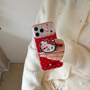 May include: Red phone case featuring a Hello Kitty design with a white face, red bow, and star pattern. The case has a clear border and includes the text "I ❤️ KT".
