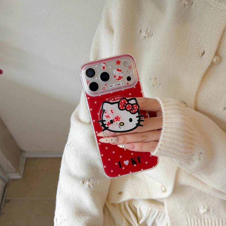 May include: Red phone case featuring a Hello Kitty design with a white face, red bow, and star pattern. The case has a clear border and includes the text "I ❤️ KT".