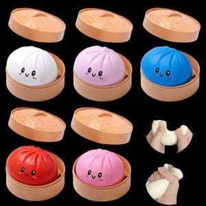 May include: A collection of colorful, squishy bao buns in bamboo steamers. The buns are white, pink, red, and blue, each with a smiling face. The image also shows a person squeezing a white, doughy substance.