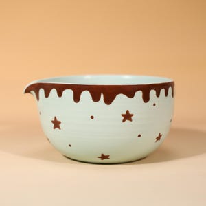 May include: A light mint green ceramic mixing bowl with a pouring spout. The rim features a brown drip pattern, and the exterior is decorated with small brown stars and dots scattered across the surface of the bowl in a repeating pattern.