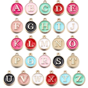 Puede incluir: Una colección de colgantes de alfabeto coloridos. Cada colgante es de un color diferente, con un borde dorado y una letra en el centro. Los colgantes son redondos y tienen un lazo en la parte superior para sujetarlos a un collar o pulsera.