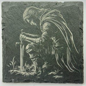 May include: Square slate coaster featuring a detailed engraving of a kneeling figure in medieval armor, holding a sword. The design is in white against a dark gray background, with grassy details at the base. A unique home decor item.