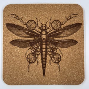 May include: Square cork coaster featuring a steampunk-style dragonfly design. The dragonfly is brown with intricate details, including gears and mechanical elements. The coaster has rounded corners and a natural cork color.