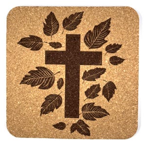 May include: Square cork coaster featuring a dark brown cross design surrounded by detailed leaf illustrations. The coaster has a natural, light brown background and is suitable for home decor.