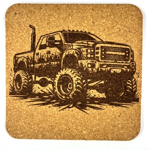 May include: A square cork coaster featuring a detailed, dark brown illustration of a monster truck. The truck has large tires, a raised suspension, and a smoke stack. The design is etched into the cork.