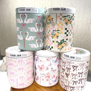 May include: A collection of five stainless steel insulated food jars, each with a 32oz capacity. The jars feature various decorative patterns, including swans, citrus fruits, bows, butterflies, and floral designs. The jars are cylindrical with white lids.