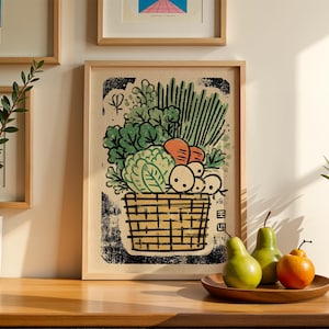 May include: A framed art print depicts a basket overflowing with vegetables, including carrots, radishes, and leafy greens. The artwork is in a woodcut style, with a black and beige color palette. Two green pears and an orange fruit sit on a wooden plate.