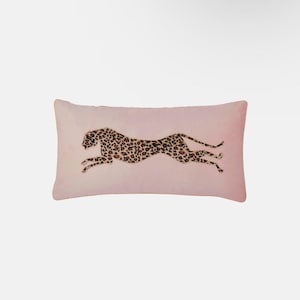 May include: A rectangular blush pink cushion with a running cheetah design. The cheetah is rendered in a brown and tan leopard print pattern. The cushion is made of a soft, plush material, suitable for a bed or sofa.