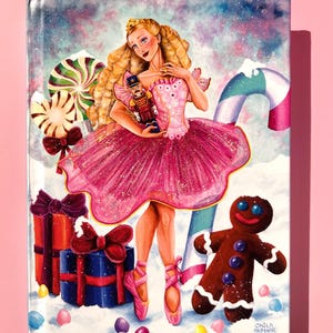 May include: A painting of a ballerina in a pink tutu holding a nutcracker, surrounded by candy canes, gifts, and a gingerbread man. The artwork has a winter holiday theme with a pink background.