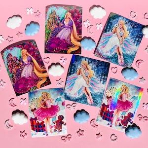 Puede incluir: Cinco impresiones artísticas con ilustraciones de una mujer rubia con vestidos de princesa, sobre un fondo rosa. Nubes, estrellas y corazones decorativos rodean las impresiones. Las impresiones miden aproximadamente 10 cm x 15 cm.