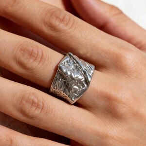 Peut inclure: Une large bague en argent présentant une surface très texturée et irrégulière qui ressemble à du métal froissé. L'anneau possède une finition polie et réfléchissante avec des indentations profondes et des crêtes sur toute la circonférence.