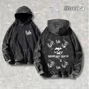 Op de afbeelding: Zwarte hoodie met de bandnaam "KoЯn" in het wit op de voor- en achterkant. De achterkant heeft een schedelafbeelding en de tekst "Falling Away From Me". De hoodie heeft een verweerde, gewassen uitstraling.