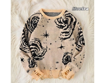 May include: Beige sweater with black swirling patterns and star designs. The sweater has a crew neck, distressed details at the hem and cuffs, and the word "Hovira" in the upper right corner.