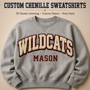 Peut inclure: Un sweat-shirt gris à col rond avec le texte CUSTOM CHENILLE SWEATSHIRTS 3D Varsity Lettering • Custom Names • Team Style en haut. Au centre, le mot WILDCATS est écrit en lettres chenille crème arquées avec des bordures marron, et le nom MASON est inscrit en dessous en lettres capitales marron.