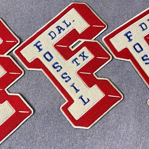 May include: Three identical embroidered patches in the shape of the letter F. Each patch features a red border, a cream-colored center, and blue embroidered text that reads F. DAL. FOSSIL TX. The patches have a textured, fabric-like appearance.