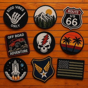 Pode incluir: Uma coleção de nove emblemas bordados com vários designs, incluindo uma mão esquelética com o texto GOOD VIBES ONLY, uma paisagem de montanha, uma placa da Rota 66, um veículo todo-o-terreno, um crânio com um raio, palmeiras, um vaivém espacial, um emblema de estrela alada e uma bandeira americana.