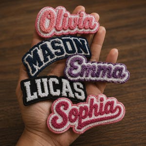 以下が含まれることがあります： Olivia、Mason、Emma、Lucas、Sophiaという名前が刺繍された5つのシェニール織ワッペン。ピンク、ネイビーブルー、パープル、ブラックなど様々なフォントと色で構成されており、白い縁取りと質感のある布地が特徴です。