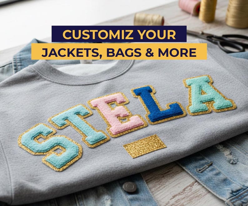 May include: A grey sweatshirt with the name "STELLA" appliqu&eacute;d in blue, pink, and teal letters with gold glitter trim. The text "CUSTOMIZE YOUR JACKETS, BAGS & MORE" is displayed in a banner above the name.