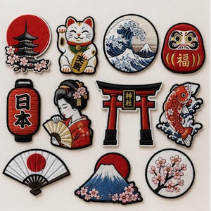 May include: A collection of eleven embroidered patches featuring Japanese motifs including a pagoda, a beckoning cat, a wave, a Daruma doll, a red lantern with Japanese text, a person with a fan, a torii gate, a koi fish, a folding fan, and cherry blossoms.