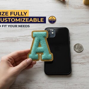 May include: A teal letter "A" patch with a gold border is held near a black smartphone. The patch is on a light-coloured surface. Text in the image reads "SIZE FULLY CUSTOMIZEABLE TO FIT YOUR NEEDS."