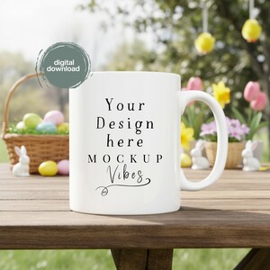 May include: White ceramic mug with the text "Your Design here MOCKUP Vibes" in black. The mug is on a wooden table with a blurred background of Easter decorations, including a basket of eggs and flowers.