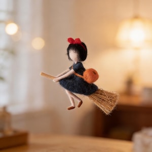 May include: A handmade felt doll of a witch riding a broom. The doll has black hair, a red bow, and a dark blue dress. An orange satchel is attached to the doll's back. The broom is made of straw and the doll is in mid-flight.