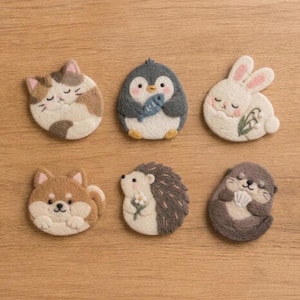 Pode incluir: Um conjunto de seis figuras de animais em lã feltrada, incluindo um gato malhado, um pinguim segurando um peixe, um coelho branco com flores, um cão castanho, um ouriço segurando uma flor e uma lontra segurando uma concha, em lã macia.
